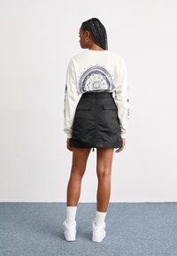 Long-sleeve cream shirt with blue graphic design; black, textured mini skirt with back zipper and pockets; white sneakers with ankle socks.
