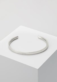 Sølv armbånd med en glatt, avrundet design. Har en polert overflate med en lett teksturert finish langs kantene.
