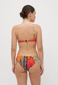Bikiny s barevným grafickým potiskem; obsahují tenké ramínka, zapínání na zádech a vzorovaný design zahrnující oranžovou, žlutou a černou.