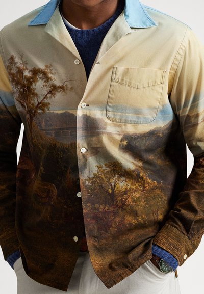 Medvilnės mišinio marškiniai su mygtukais, papuošti kraštovaizdžio atspaudu žemės tonų spalvomis. Šviesiai mėlyna apykaklė ir kišenės detalė.