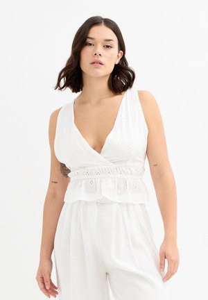 Top sin mangas blanco con un profundo escote en V, cintura fruncida con un borde de volantes y detalles de bordado de ojal. Tela suave y ligera.