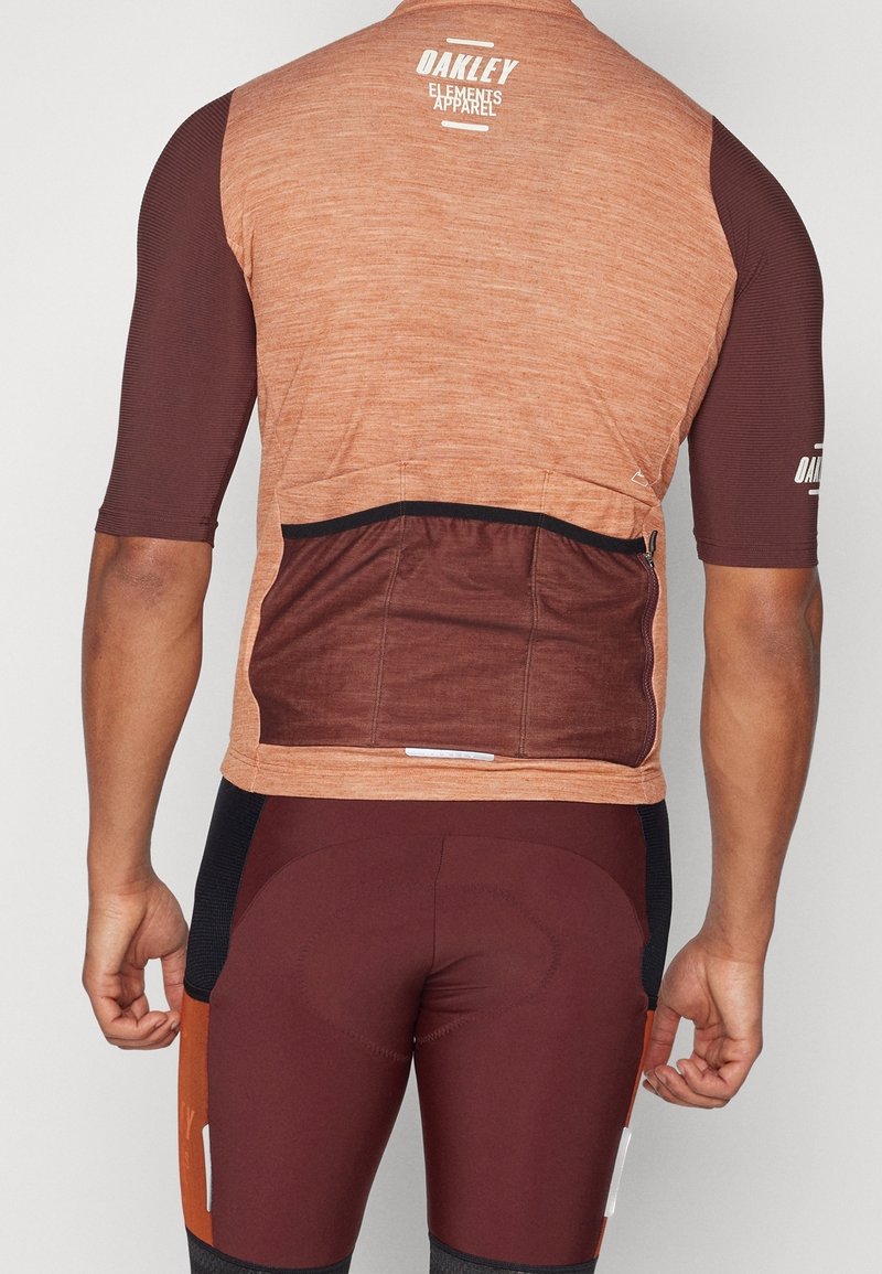 Hombre vestido con un maillot de ciclismo marrón y óxido con bolsillos traseros y pantalones cortos de ciclismo acolchados a juego, visto desde atrás.