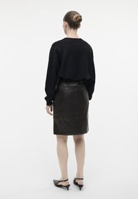 Sort oversized sweater parret med en tætsiddende, mørkebrun læderpencilskørt. Outfittet har en glat tekstur og minimalistisk design.