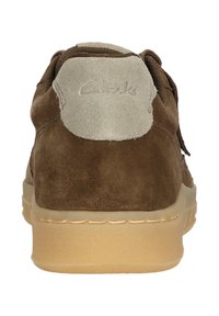 Brun mockasinsko med en krämfärgad hälla med präglad "Clarks"-logotyp. Flexibel gummisula med en strukturerad yta.