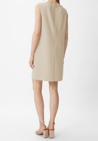 Vestido sin mangas beige con un diseño estructurado y detalle de cremallera en la parte posterior. La tela tiene un acabado texturizado con un corte recto en el dobladillo.