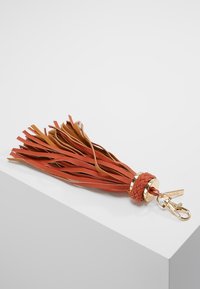 Skórzane frędzle w kolorach czerwonym i jasnobrązowym z oplecionym detalem, wyposażone w złocony, metalowy zaczep do przypięcia. Teksturowany wzór frędzli.