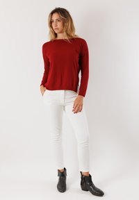 Maglietta rossa a maniche lunghe con vestibilità comoda, abbinata a pantaloni bianchi slim-fit. Completato con stivaletti neri alla caviglia con cerniere laterali.