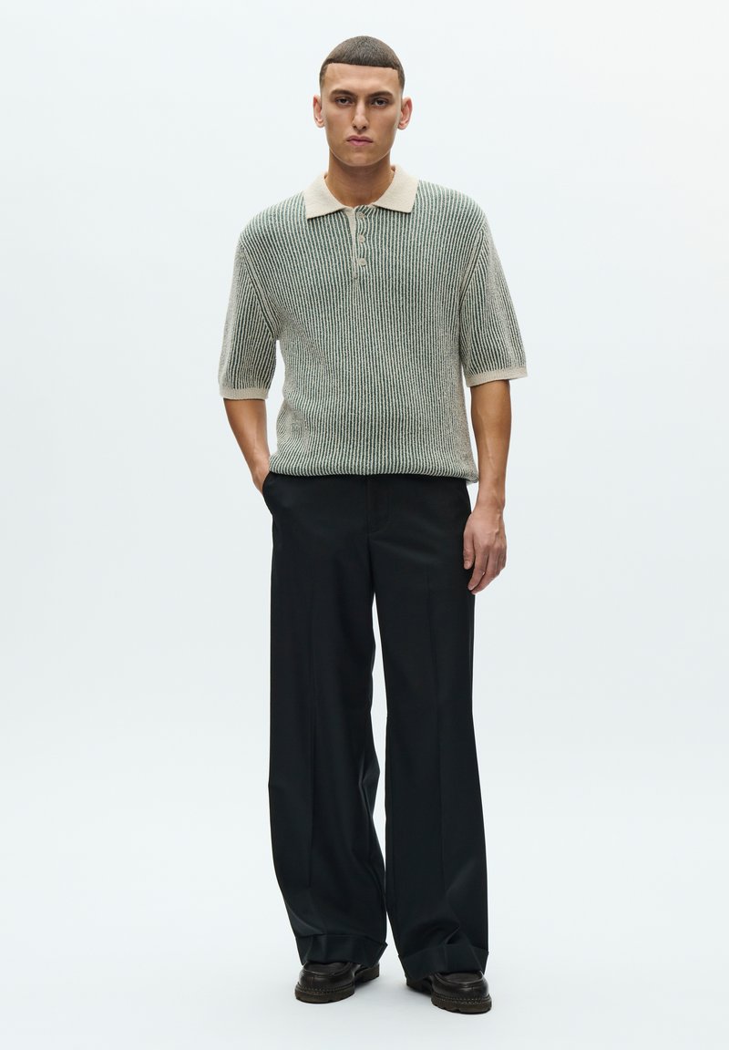 Short-sleeve polo with a ribbed texture in green and cream, paired with black wide-leg trousers. Features three-button placket and contrasting collar.