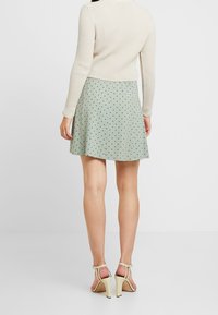 Groene polka dot rok met een uitlopende ontwerp, gemaakt van lichtgewicht stof, gecombineerd met een crème ribbelshirt met lange mouwen en beige hakken.