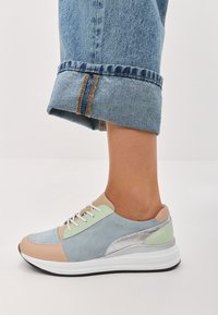 Moniväriset sneakerit, joissa on vaaleansinistä, beigeä ja vihreää nubukkia, heijastava hopeinen yksityiskohta ja valkoinen pohja. Säärettömät farkut näkyvissä.