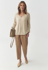 Bežinė v-viečio megztinis, laisvas prigludimas, derinamas su šviesiai rudos spalvos aptemptomis kelnėmis. Bežinės slingback bateliai. Rudos spalvos kryžminė rankinė su dirželiu.
