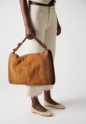 Braune Wildleder-Handtasche mit sandfarbenen Lederakzenten, rechteckige Form, doppelte Griffe und Reißverschluss, kombiniert mit cremefarbenen Hosen und beigen Ballerinas.