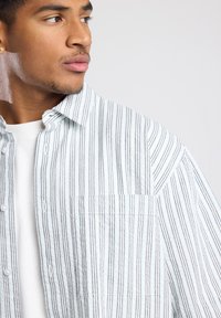 Striped shirt in white and blue fabric, featuring a button-up front, single chest pocket, and relaxed fit with a soft texture.