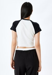 Kortogesneden top met korte mouwen, een witte ribbelige lichaamsstof en zwarte raglanmouwen. Gecombineerd met zwarte hoge taillebroek met een witte elastische tailleband.