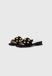 Black suede slide-on shoes featuring gold metal studs on the upper, an open toe design, and a low black triangular heel.