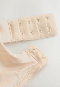 Beige bh med lukning på ryggen med fire rækker hægter og justerbare stofbånd på hvid baggrund.