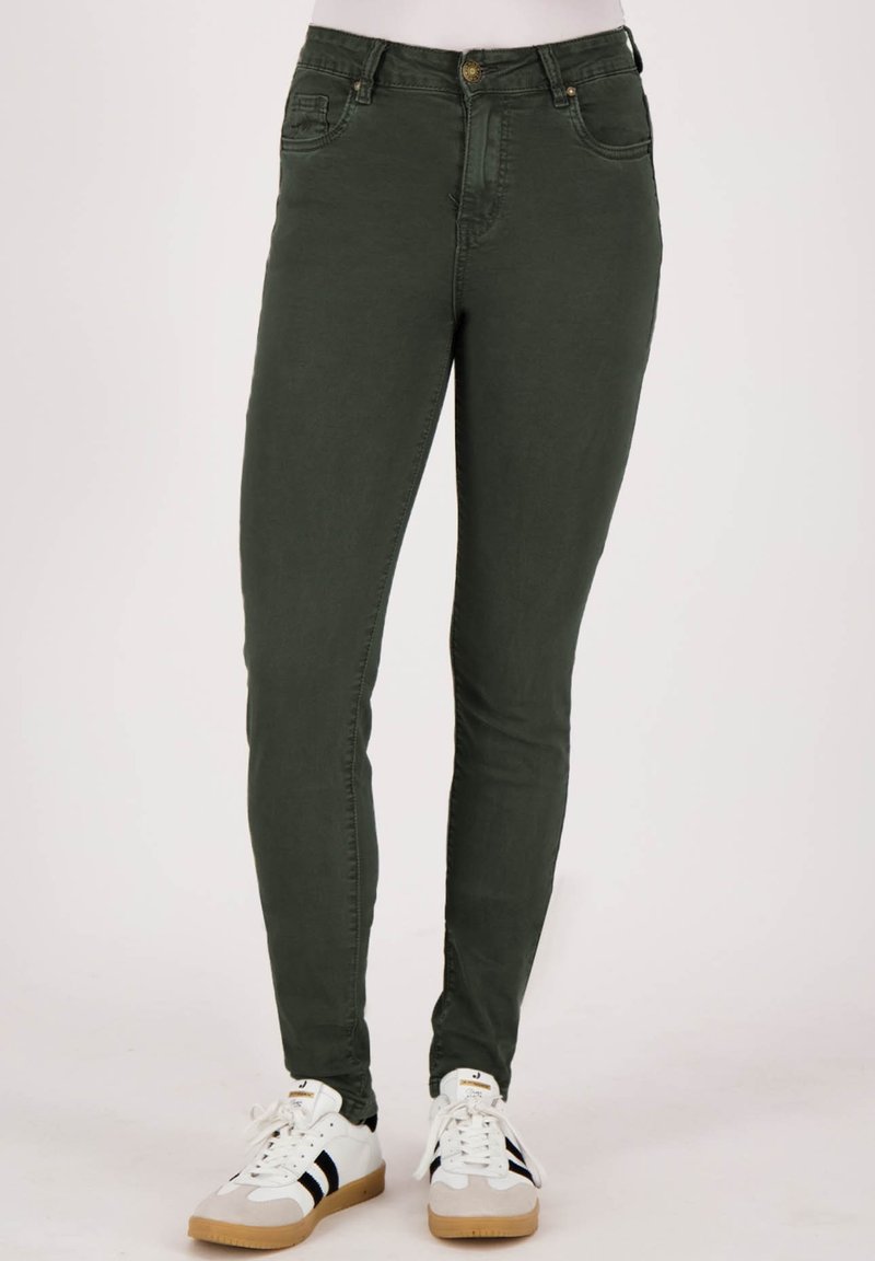 Olijfgroene skinny jeans met een gladde textuur, vijf-pocket ontwerp en knoopsluiting, gecombineerd met witte sneakers met zwarte strepen.