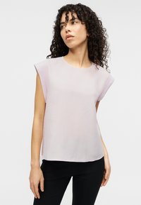 Ανοιχτό ροζ μπλούζα με κοντά μανίκια, απαλό ύφασμα, στρογγυλή λαιμόκοψη και άνετη γραμμή, συνδυασμένη με στενά μαύρα παντελόνια.