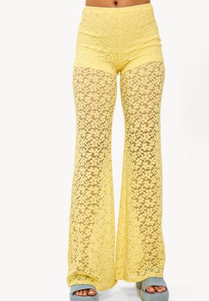 Pantalones acampanados de encaje amarillo con un diseño transparente, que presentan una cinturilla alta y un patrón floral en toda la prenda. Destacan por su textura suave.
