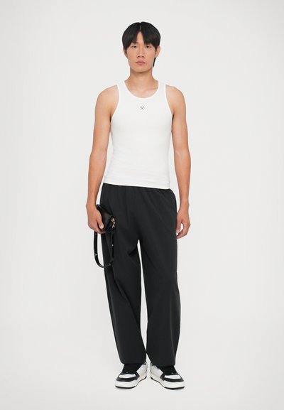 Débardeur blanc à côtes avec encolure ronde, associé à un pantalon noir ample. La personne tient un petit sac noir avec une bandoulière. Chaussures noir et blanc.