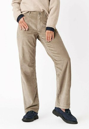 Pantaloni in corduroy beige con taglio dritto, dotati di tasche anteriori e posteriori, indossati con un maglione beige e scarpe in suede blu.