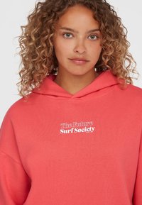 Korallenfarbener Hoodie mit lässiger Passform, mit einem Frontdesign in Weiß, das "The Future Surf Society" zeigt. Hergestellt aus weichem Baumwollmaterial.