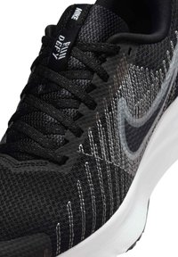 Chaussure de sport noire avec une tige en maille texturée ornée de rayures dégradées grises, des lacets noirs et une semelle intermédiaire blanche. Logo Nike visible sur la languette.