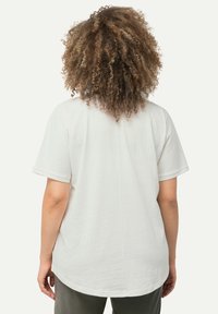 Camiseta blanca de algodón con mangas cortas, cuello redondo y dobladillo curvado. Presenta una costura central en la parte posterior. Textura suave.