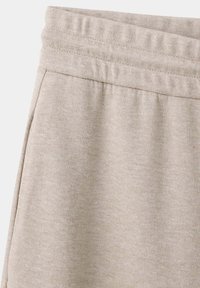Pantalon en tissu beige avec ceinture élastique et poche latérale apparente sur fond clair.