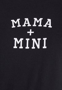 Mustat kankaiset t-paidat, joissa on valkoiset kirjaimet, jotka lukevat "MAMA + MINI" rohkealla, isoilla kirjaimilla. Silkkinen, kevyt rakenne.