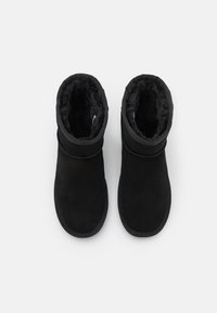Bottines noires en daim avec une doublure intérieure douce, ressemblant à de la fourrure, bout rond et poignets élastiques pour un ajustement confortable.