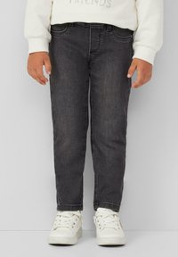 Zwarte spijkerbroek van denim met een slim fit, vijf pocket ontwerp en subtiele structuur, gecombineerd met witte sneakers. De top is een lichte sweatshirt.