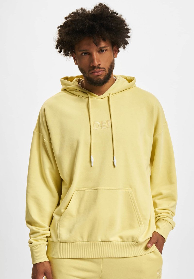 Hoodie jaune en mélange de coton doux. Comprend une poche frontale, des poignets en côte et des cordons de serrage avec des embouts en plastique blanc. Logo brodé.