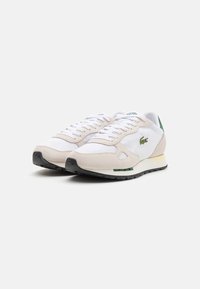 Hvit og beige sneakers med en kombinasjon av semsket skinn og mesh-materialer, rund tå, snøring, grønne detaljer og svart gummisåle.