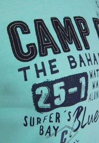T-shirt di cotone azzurro chiaro con testo e grafiche nere in evidenza, tra cui "CAMP" e "25-1", dalla texture morbida e senza modelli visibili.