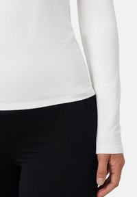 Bílé dlouhé tričko s hladkým povrchem a prošitým lemem. Černé legíny s přiléhavým střihem, které mají tónové logo na pase.