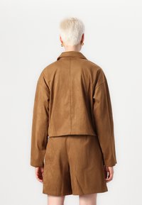 Bruine faux-suède korte jas met een omgeslagen kraag en drop schouders, gecombineerd met passende shorts en minimale stikdetails.