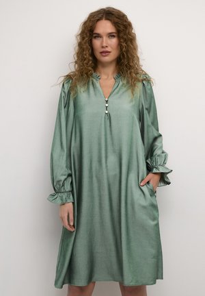 Ein grünes, knielanges Kleid aus glänzendem Stoff, mit einem V-Ausschnitt, Knopf-Akzenten und rüschigen Ärmeln sowie Taschen.