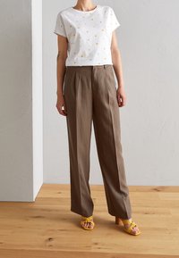 Vit t-shirt med flerfärgade prickar, kombinerad med ljusbruna, högmidjade plisserade byxor och gula klacksandaler. Naturlig trägolv.