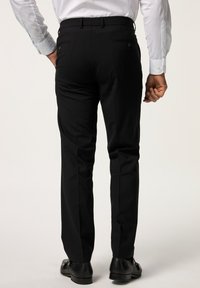 Pantaloni neri con una vestibilità su misura, dotati di due tasche posteriori e una texture liscia, abbinati a scarpe in pelle nere.