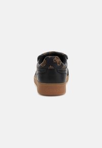 Sneaker negru cu un model texturat, având o talpă din cauciuc maro și logo-ul embosat "GUESS" pe spate. Detalii de design unice pe accente.