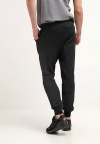 Black athletic sweatpants with elastic waistband and side pockets, made from soft material, featuring a tapered leg design and minimal detailing.