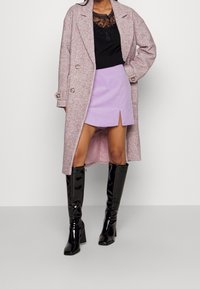 Cappotto rosa chiaro a motivo chevron sopra una camicia nera con pizzo, abbinato a una mini gonna lilla con uno spacco frontale e stivali neri lucidi alti fino al ginocchio.