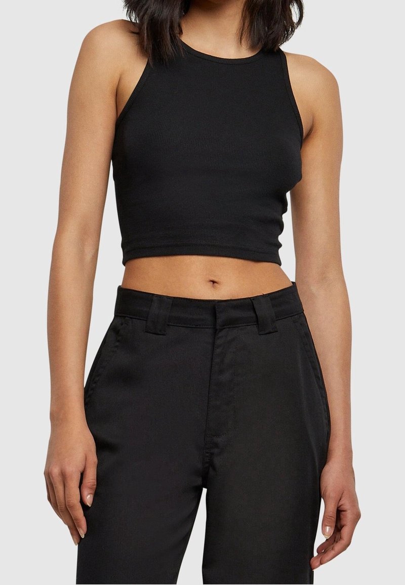 Svart ribbad crop top med hög hals och ärmlös design, parat med svarta skräddarsydda byxor. Slät textur, avslappnad passform.