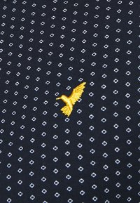 Navy fabric with a diamond pattern in white. Features a yellow embroidered bird design, adding subtle texture and detail.