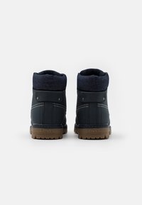 Paire de bottes Levi’s bleu foncé avec semelles en caoutchouc marron vues de dos, dotées de colliers rembourrés à la cheville et de coutures blanches.