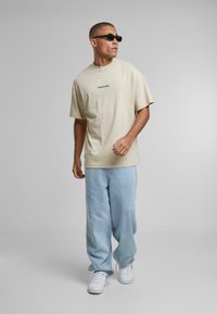 Beige bomulds t-shirt med korte ærmer og rund hals. Sammen med lyseblå, bred ben denim bukser og hvide sneakers. Sorte solbriller båret.