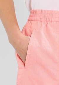 Shorts rose clair en tissu doux et texturé, dotés d'une taille élastique et de poches latérales. Vue en gros plan mettant en valeur le détail des poches.