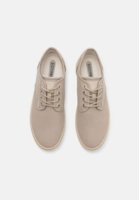 Scarpe da ginnastica in tela beige con punta rotonda, design con lacci e superficie testurizzata. Presentano suola in gomma e dettagli di cuciture sottili.