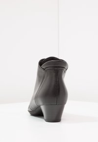 Černé kožené kotníkové boty s křivkovým designem, nízkým podpatkem a švy vzadu; hladká textura a jemné linie.